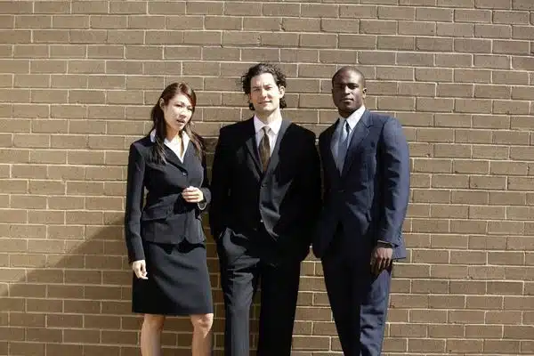 three people in business attire in front of a brick wall