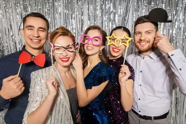 group of men and women posing in front of photobooth backdrop with props